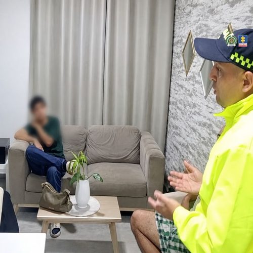 Policía conversa con una persona sentada en un sofá, cuyo rostro aparece difuminado, durante el procedimiento en Pereira.
