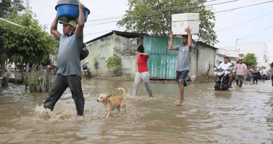 Personas cruzan una calle inundada mientras transportan sus pertenencias durante las recientes lluvias en Colombia.